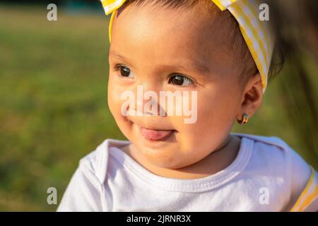 detail shot of a beautiful brown-skinned latina baby girl, showing her tongue on a beautiful summer day, with her very happy look. family concept. Stock Photo