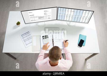 Young Businessman Calculating Invoice On Computer Screen Using Calculator Stock Photo