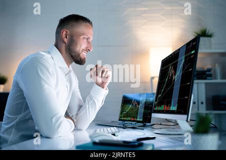 Successful Stock Market Trader Looking At Graphs On Multiple Screens In Office Stock Photo