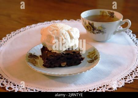 Delicious dessert of a chocolate brownie and ice cream with a cup of tea in porcelain china. Stock Photo