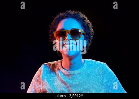 african woman in sunglasses over neon lights Stock Photo