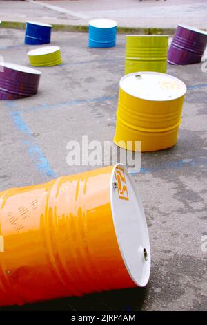 Artistic installation of colorful metal barrels that rest and intersect on an asphalt street. Conceptual image, urban intervention. Stock Photo