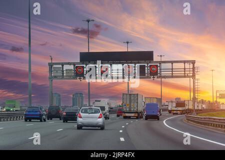 Dense stream of trucks and cars on a highway with speed signs of 110 km per hour in the evening at sunset Stock Photo