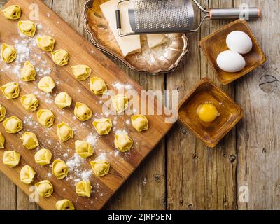 Homemade dumplings with meat filling are laid out on a wooden cutting board sprinkled with flour. Ingredients, kitchen utensils on a wooden background Stock Photo