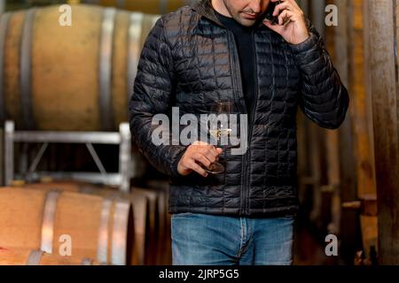 Man in the wine cellar with barrels in background drinking and tasting wine. Stock Photo