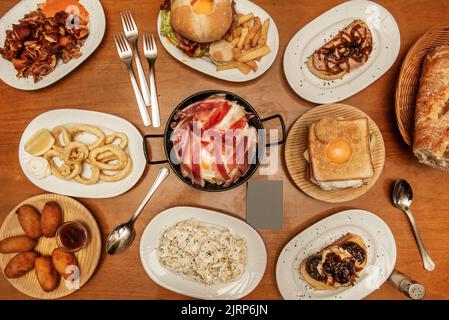 Plates and trays of typical recipes of Spanish gastronomy with croquette tapas, grilled ear, alioli potatoes, Andalusian squid, toast, sandwich with f Stock Photo