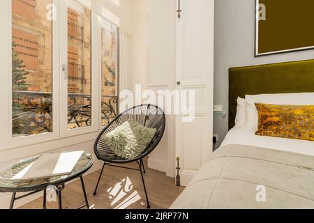 Bedroom with light green velvet upholstered headboard, gold cushions, bay window with white aluminum windows, hammock with green cushion and matching Stock Photo