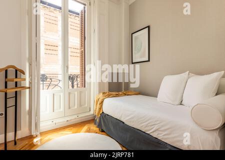 Bedroom with light green velvet upholstered headboard, gold cushions, bay window with white aluminum windows, hammock with green cushion and matching Stock Photo