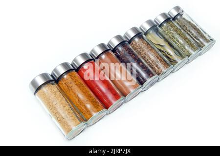 The different types of spices and herbs stored inside the small closable glass bottle isolated on a white background. Stock Photo