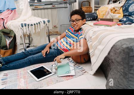 Black boy in eyeglasses laughing while sitting on floor at home Stock Photo