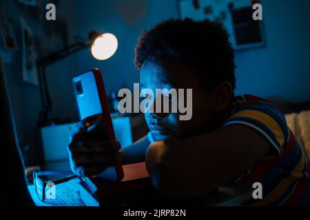 Black boy using mobile phone while sitting by computer screen in home Stock Photo