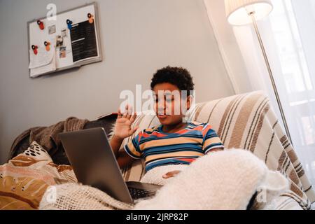 Black boy gesturing and using laptop while sitting on sofa at home Stock Photo