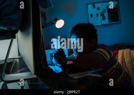 Black boy using mobile phone while sitting by computer screen in home Stock Photo