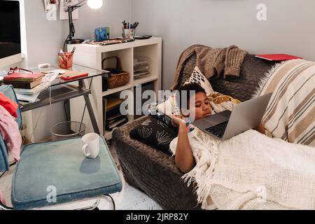 Black boy working with laptop while lying on sofa at home Stock Photo