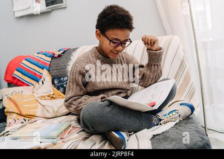 Black boy using mobile phone and doing homework on sofa at home Stock Photo