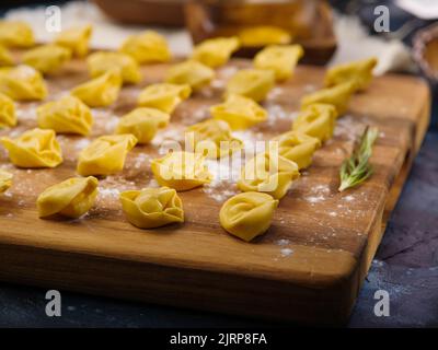 Homemade dumplings, ravioli on a wooden cutting board with a sprig of rosemary are waiting to be cooked. Close-up. Italian, Chinese cuisine. Recipes f Stock Photo