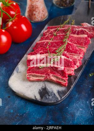 On a dark blue background, raw meat steaks from organic meat from the farm and ripe red tomatoes. The process of cooking meat steaks from beef, veal, Stock Photo