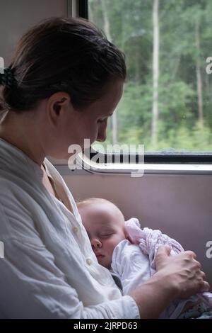 Caucasian baby sleeping traveling by train on mother lap Stock Photo