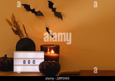 Home Halloween decor composition with candle, black pumpkin, bats and light box with text boo Stock Photo