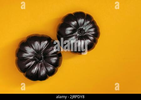 Two black pumpkins on bright orange background, Halloween decor, top view Stock Photo