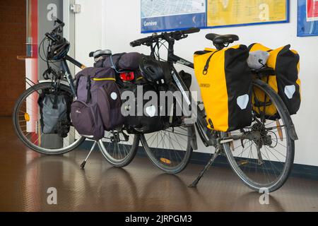 Two touring bicycles, heavily laden with cycle / bike panniers, left standing by their cycle riding owners at a train station on the French and Swiss border between France Switzerland. (131) Stock Photo