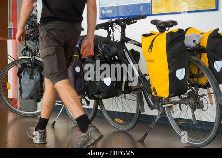 Two touring bicycles, heavily laden with cycle / bike panniers, left standing by their cycle riding owners at a train station on the French and Swiss border between France Switzerland. (131) Stock Photo