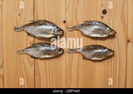 Dried salted fish on a wooden background. The fish is completely salted with the head and viscera. Stock Photo