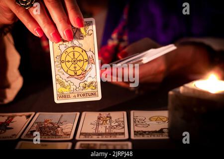 Fortune teller female hands showing The Wheel of Fortune tarot card, symbol of good luck, during a reading. Close-up with candle light, moody atmosphe Stock Photo