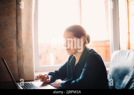 Happy smiling mature woman using laptop computer while working at home Stock Photo