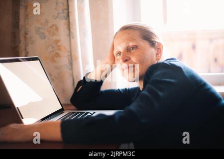 Thoughtful woman leaning at desk sitting by laptop computer at home Stock Photo