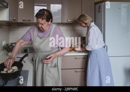 Two women, mother and daughter, are cooking pies in the kitchen. Stock Photo