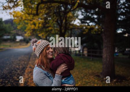 Mom smiling and holding toddler walking outside under a yellow f Stock Photo