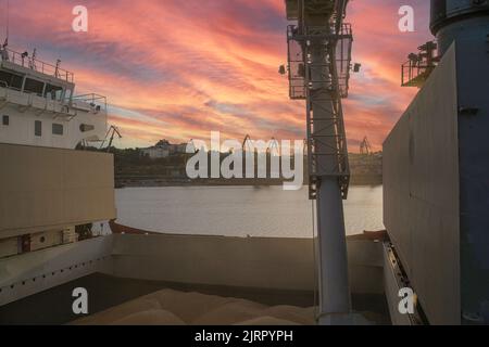 loading corn onto a bulk carrier ship in the port at the grain terminal. Port grain elevator. Industrial sea trading port bulk cargo zone grain termin Stock Photo