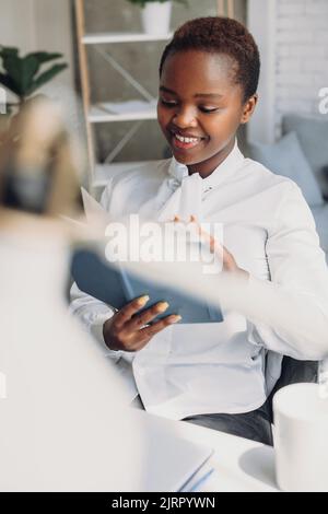 Casual smiling african-american businesswoman looking in her diary while sitting in her office. Reading interesting article online. Weekend activities Stock Photo