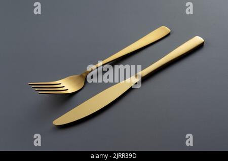 Gold knives and forks set against a black background. Beautiful gold cutlery. Stock Photo