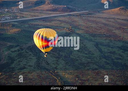 A colorful hot air balloon floats above a lush desert landscape in the light of early morning Stock Photo