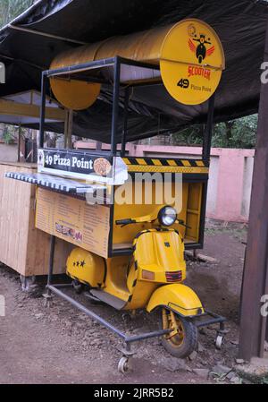 Old yellow scooter used as a prop for road side stall selling fast food and pizzas. Location: Nashik, Maharashtra, India. Date - July 03 2022 Stock Photo