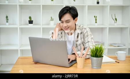 Smart and handsome young Asian male freelancer remote working in the coffee shop, using his portable laptop computer. Stock Photo