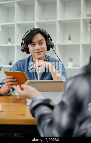 Portrait, Handsome young Asian male radio host interviewing his special guest in the studio. Broadcasting and podcasting concept Stock Photo