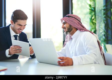 Keeping business collaborative and productive. a young muslim businessman using a laptop and digital tablet with his colleague at work. Stock Photo