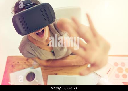 Be amazed by full immersion into the digital world. High angle shot of a young businesswoman wearing a VR headset while working in an office. Stock Photo