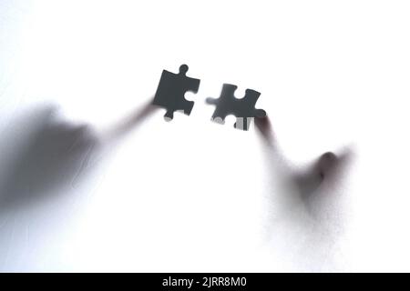 Fitting the pieces together. two unrecognizable people holding two puzzle pieces together. Stock Photo