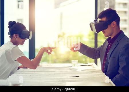 Testing their ideas through the simulated world. two businesspeople wearing VR headsets while working together in an office. Stock Photo