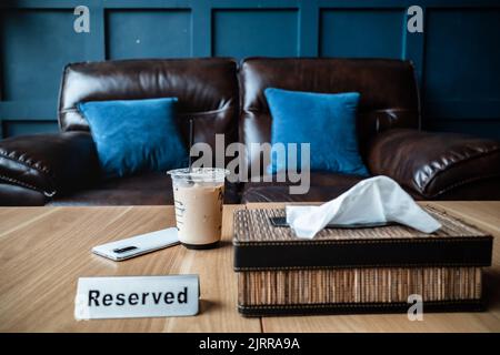 A Cup of Iced Coffee on a Reserved Table at Restaurant with Leather Sofa and Blue Cushions on the Background Stock Photo