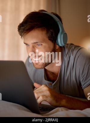 Laptop, online tv and movie subscription with headphones late at night in his bedroom. Man with insomnia distracted with steaming internet to watch Stock Photo
