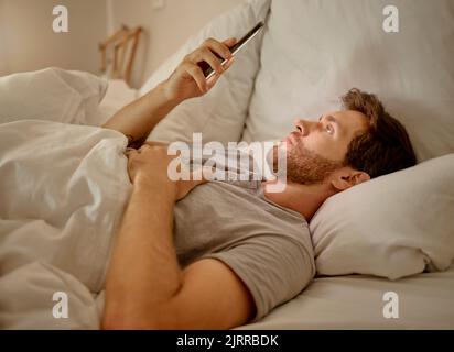 Social media, mobile app and relax man with smartphone using the internet or online website content at night in his bedroom with home wifi. Serious Stock Photo