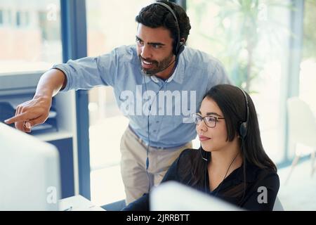 Resolving issues for their clients together. two call centre agents working together in an office. Stock Photo