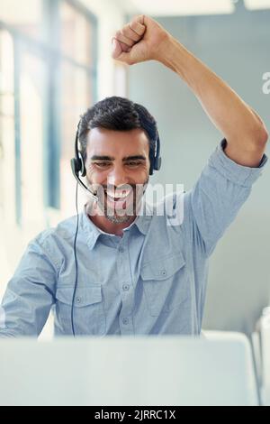 Hes surpassed his sales target. a call centre agent doing a fist pump while working on a laptop in an office. Stock Photo