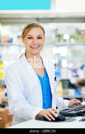 Happy to assist you. a young pharmacist using a computer at the checkout counter. Stock Photo