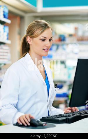 Keeping a close eye on her customers records. a young pharmacist using a computer at the checkout counter. Stock Photo
